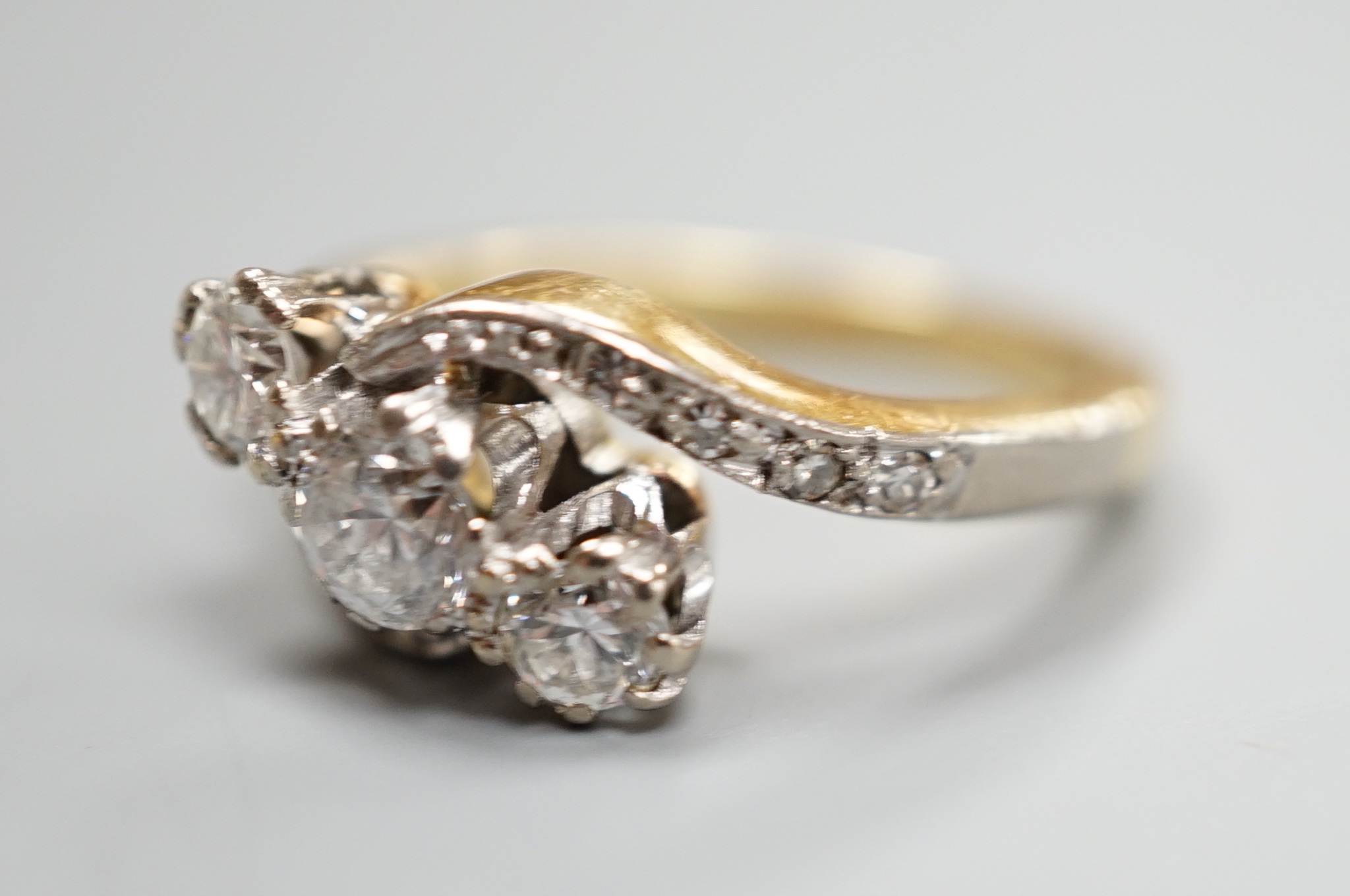 A yellow metal and three stone diamond set crossover ring, with diamond set shoulders, size I, gross 4.6 grams.